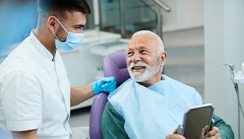 Senior patient looking at dentist while holding small mirror