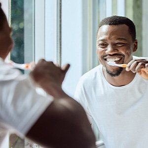 Man smiling while brushing his teeth in bathroom