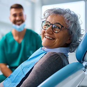 Woman with glasses smiling while sitting in the dental treatment chair