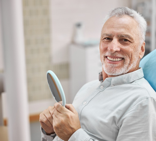 Senior man smiling in the dental chair while holding a mirror