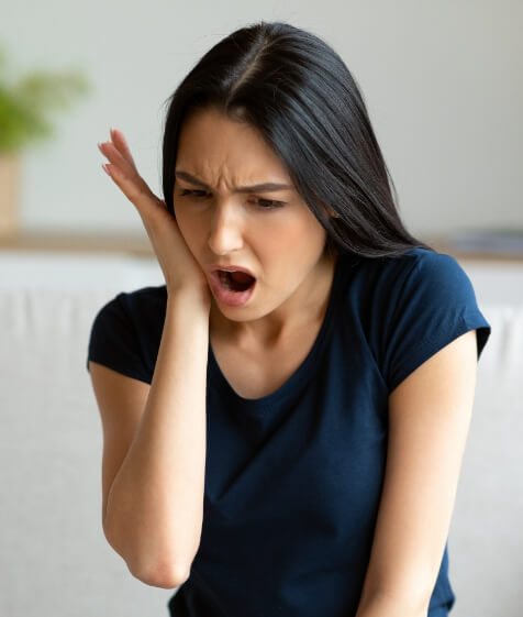Woman holding her cheek in pain before seeing an emergency dentist in Medford