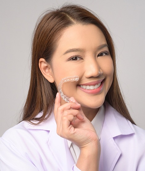 Smiling patient holding clear aligner