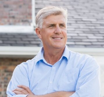 Man in a light blue collared shirt smiling outdoors
